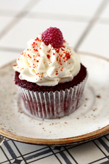 Homemade bakery style red velvet delicious sponge cupcake with white butter cream cream frosting and on raspberrie top on plate. Candy bar for celebrating partys and birthdays