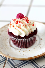 Homemade bakery style red velvet delicious sponge cupcake with white butter cream frosting and on raspberrie top on plate. Candy bar for celebrating partys and birthdays