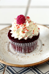 Homemade bakery style red velvet delicious sponge cupcake with white butter cream cream frosting and on raspberrie top on plate. Candy bar for celebrating partys and birthdays