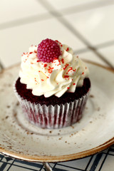 Homemade bakery style red velvet delicious sponge cupcake with white butter cream cream frosting and on raspberrie top on plate. Candy bar for celebrating partys and birthdays