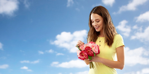 birthday and people concept - smiling young woman or teenage girl in yellow t-shirt with flower bouquet over blue sky and clouds background