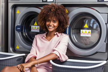 Young black African American woman waiting her clothes to be washed in a automatic laundry