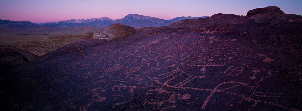 BISHOP, CALIFORNIA - 2012: Sky Rock petroglyphs near Bishop, California, during sunset with the Sierra Nevada mountain range in the distance. Located in the Volcanic Tablelands region, these ancient Native American petroglyphs are believed to have been created by the ancestors of what are today known as the Owens Valley Paiute tribe.