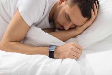 people, technology and rest concept - close up of man with smart watch sleeping in bed