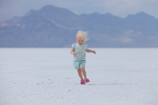 Little blonde female toddler running awkwardly across the Utah salt flats 