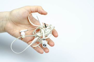 tangled white no brand earphones in a hand on white