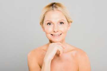 attractive and smiling mature woman touching her face and looking at camera on grey background