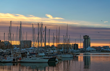 Barcelona, Spain-January 02, 2016: Early morning in port in Barcelona. Yachts moored in port. Beautiful sun rising sky at the background