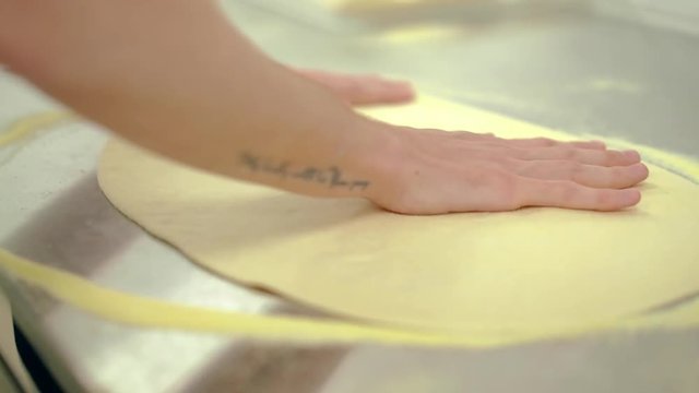 CU: Cock rolls out pizza dough with his hands.