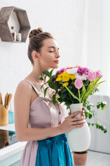 pretty smiling girl with closed eyes smelling bouquet of wildflowers in vase