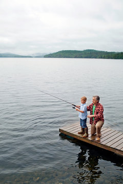 Senior man showing grandson how to fish off jetty 
