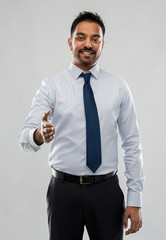 business, office worker and people concept - smiling indian businessman stretching hand out for handshake over grey background
