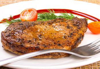 Steak meat with tomato and lettuce salad leaf and fork in a white plate