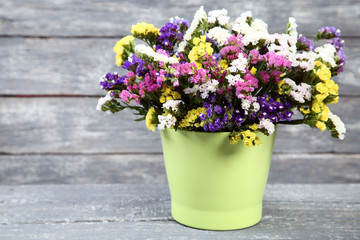Spring flowers in green pot on grey wooden table