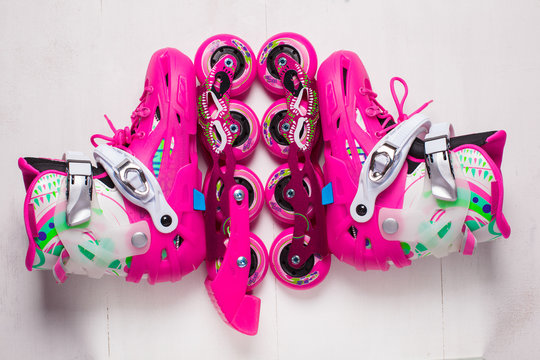 A pair of pink stylish roller skates on a white wooden background