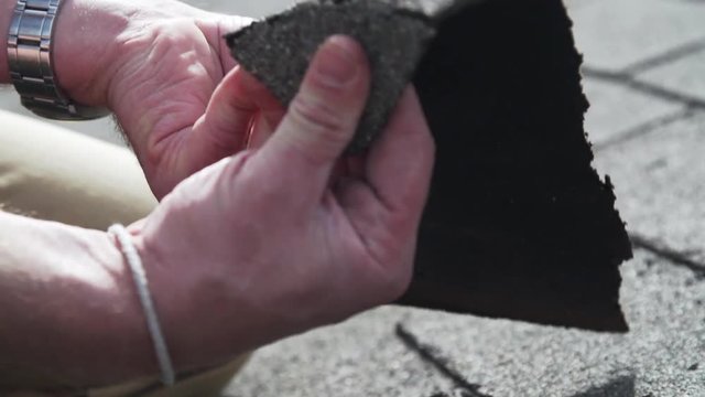 Roof inspector cracking old asphalt shingles during residential inspection