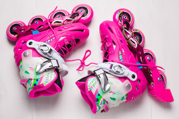A pair of pink stylish roller skates on a white wooden background