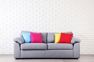 Modern grey sofa with colorful pillows on brick wall background