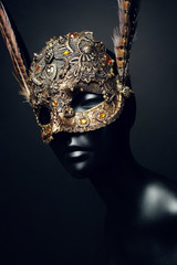 Black head of mannequin in creative metal mask with jewels and feathers