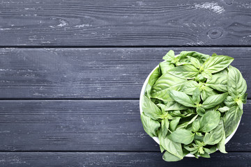 Green basil leafs in bowl on black wooden table