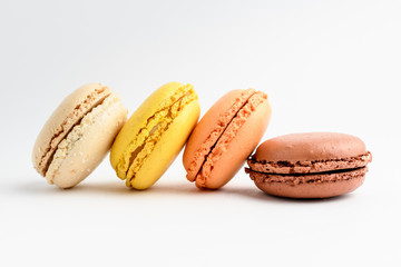 Side view of four sweet French macarons isolated on white, flavours of coconut, vanilla, lemon, orange, caramel and chocolate
