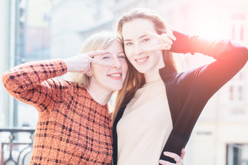 Portrait of two trendy female mature mother with her adult daughter posing with peace sign. Stylish women having fun during sunny morning. Close up. Happy loving family concept. Sun glare effect