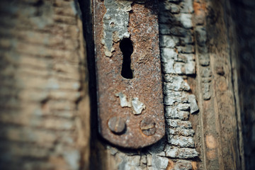 Old metal keyhole on the wooden door, which crumbles paint and which is in an abandoned state