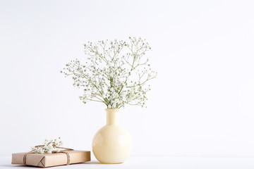 White gypsophila flowers in vase with gift box on grey background