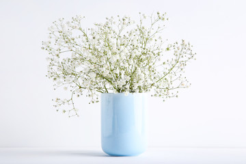 White gypsophila flowers in blue cup on grey background