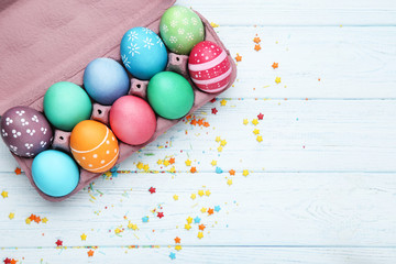 Colorful easter eggs in carton box with sprinkles on wooden table