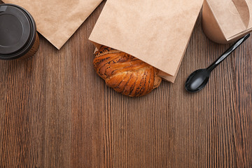 Bun in paper bag and takeaway food on wooden background, top view with space for text