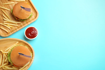 Tasty burgers, French fries and sauce on color background, top view with space for text. Traditional American food
