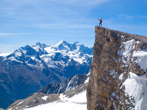 A male mountaineer is standing on top of the Barrhorn in the Swiss Alps. 