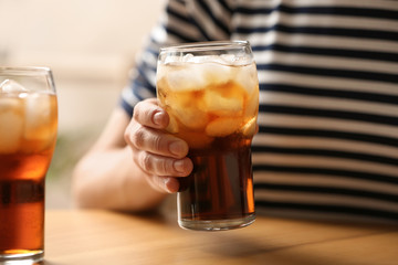 Woman holding glass of cola with ice at table, closeup