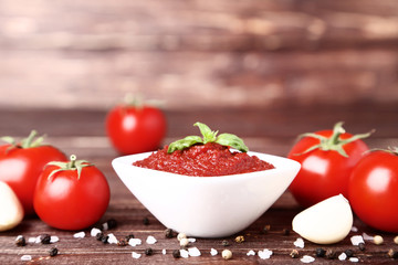 Ketchup in bowl with spices and garlic on brown wooden table