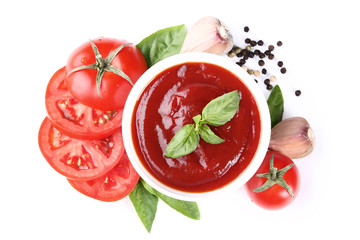 Ketchup in bowl with tomatoes and basil leafs isolated on white background