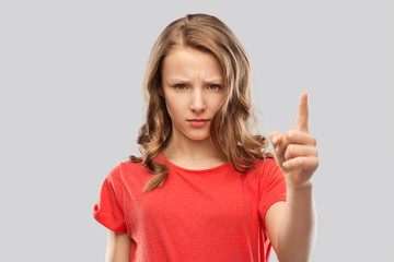 warning, attention and people concept - angry frowning teenage girl pointing finger up over grey background