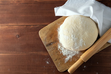 Classic wooden rolling pin with freshly prepared dough and dusting of flour on wooden background