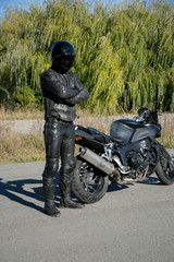 Naklejka premium The motorcyclist in black wearing a helmet looks at a motorcycle