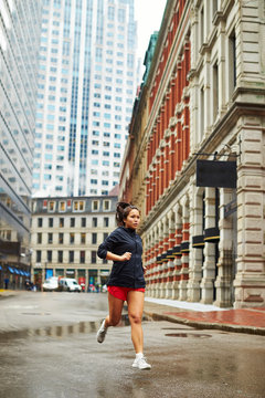 A young asian girls runs through the wet city streets of Boston.