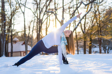 Woman standing with bent knee and arm raised while doing yoga outdoors in winter