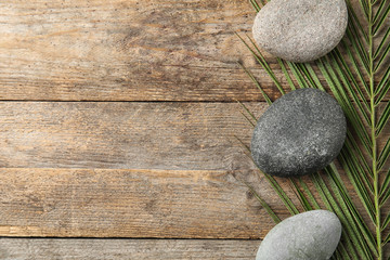 Zen stones and tropical leaf on wooden background, top view with space for text