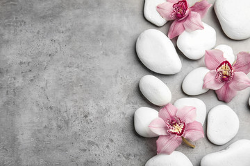 Zen stones and exotic flowers on grey background, top view with space for text