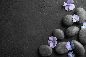 Zen stones and exotic flowers on dark background, top view with space for text