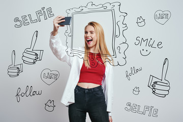 Selfie time! Cheerful young woman with blond hair making selfie by her smartphone and giving a wink...