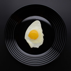 Fried egg on a stylish black plate. Breakfast. Awesome black background. Stylish design. Egg white and yolk. Top view. Organic food. Space for a text.