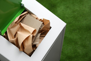 Trash bin with paper and cardboard on color background, space for text. Recycling concept