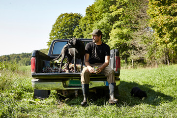 A farmer and his dog sit in his truck after harvesting vegetables.