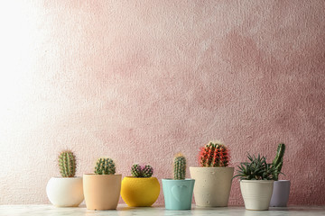 Different potted cacti on table near color background, space for text. Interior decor