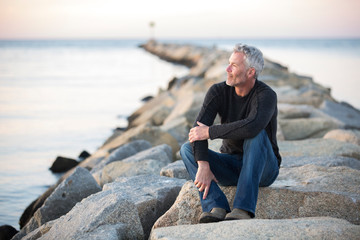 Gray-haired man contemplating on coastal rocks at dusk, Dennis, Massachusetts, USA